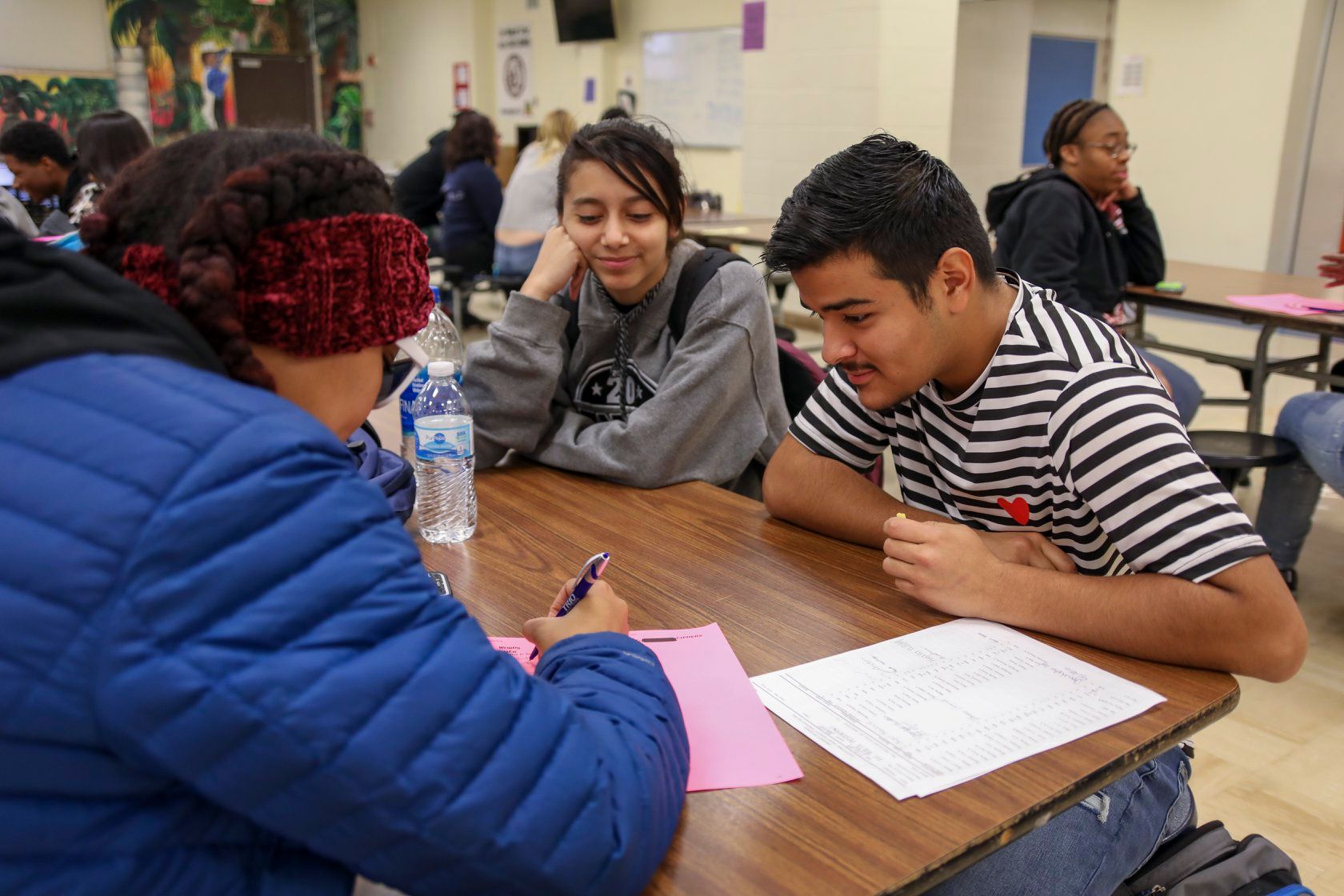 Two high school seniors sitting in a cafeteria working with an adult