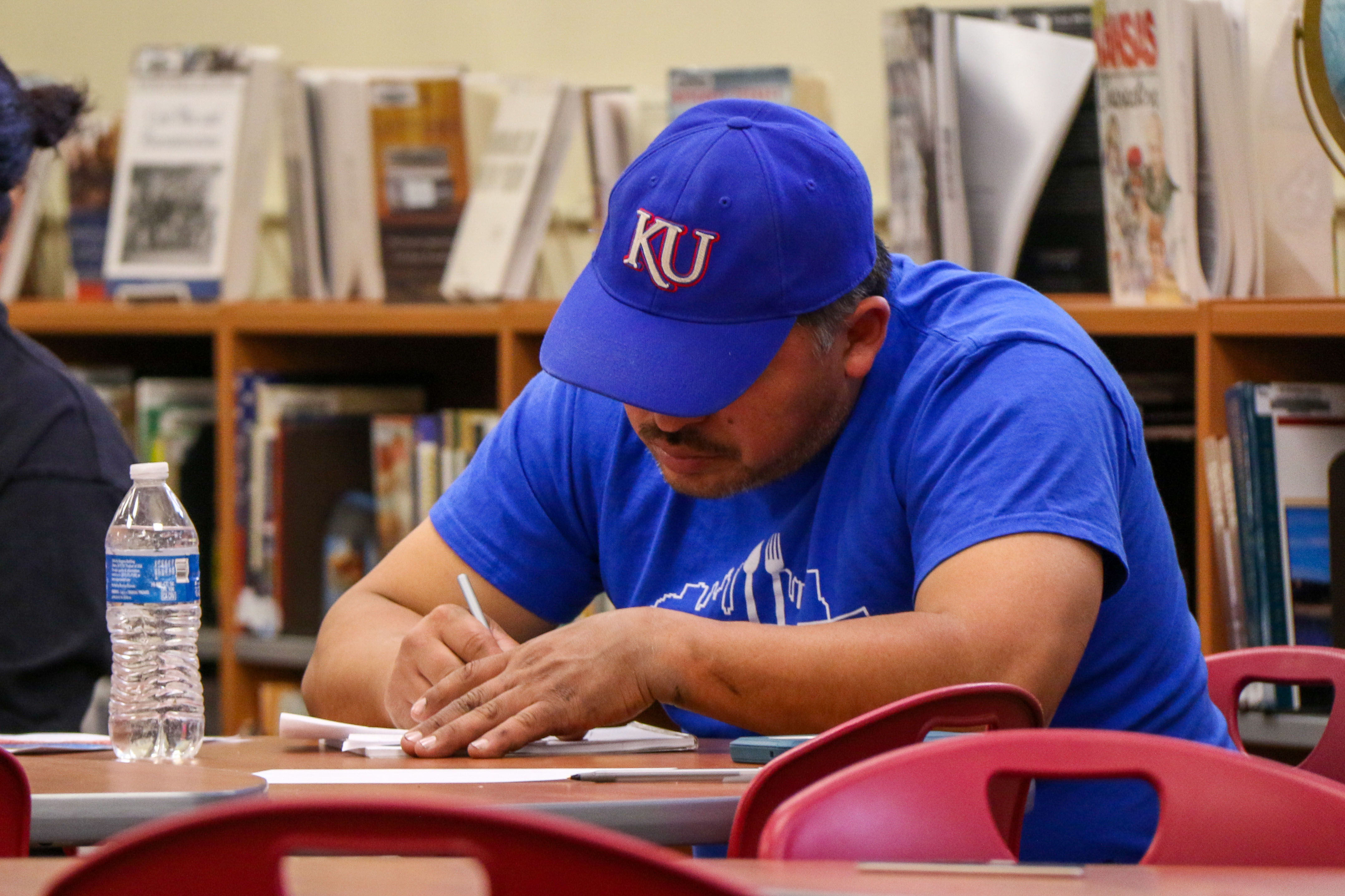 A parent in a workshop writing on paper wearing a KU hat
